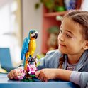 Een meisje met vlechtjes kijkt naar een gele en blauwe papegaai van LEGO-blokjes op een tak met roze bloemen.