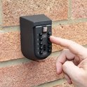 Hand die een zwarte metalen sleutelkluis op een bakstenen muur bedient. Cijfer 9 wordt ingedrukt.
