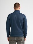 Man van achteren gezien in een blauw vest met ritssluiting en grijze jeans.