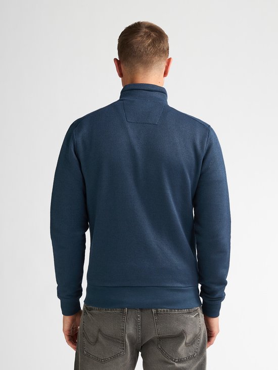 Man van achteren gezien in een blauw vest met ritssluiting en grijze jeans.