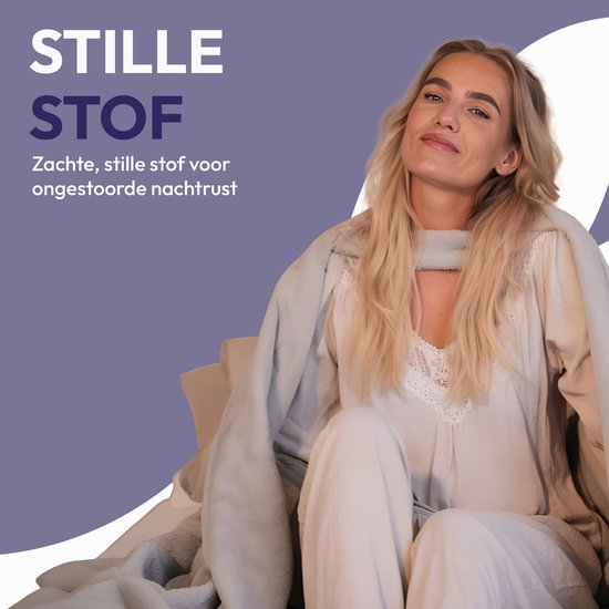 Een vrouw met blond haar zit op de bank, omhuld door een zacht, grijs dekbed.