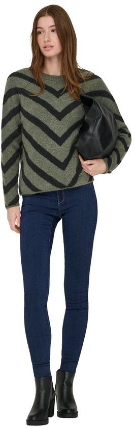 Model met olijfgroene trui met zwarte V-strepen, spijkerbroek en zwarte tas.