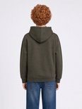 Jongen met krullend rood haar, van achteren gezien, in een donkergroene hoodie en blauwe jeans.