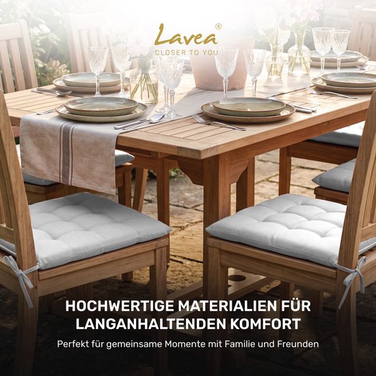 Een gedekte eettafel met lichtgrijze stoelkussens op houten stoelen, buiten.