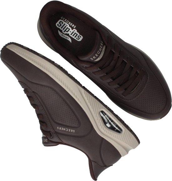 Twee donkerbruine Skechers sneakers, de ene met zool omhoog, de andere plat.