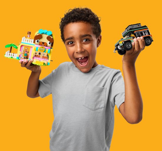 Garçon aux cheveux bouclés en t-shirt gris tenant une animalerie rose et une jeep, toutes deux en LEGO.