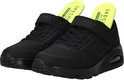 Paar zwarte Skechers sneakers met klittenbandsluiting en neongele binnenzolen met tekst.