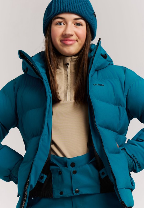Close-up van een meisje in een blauwe ski-jas, beige trui en blauwe muts. "protest" logo op de jas.