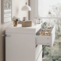 Witte commode met een opengesperde lade met gouden cosmetica.