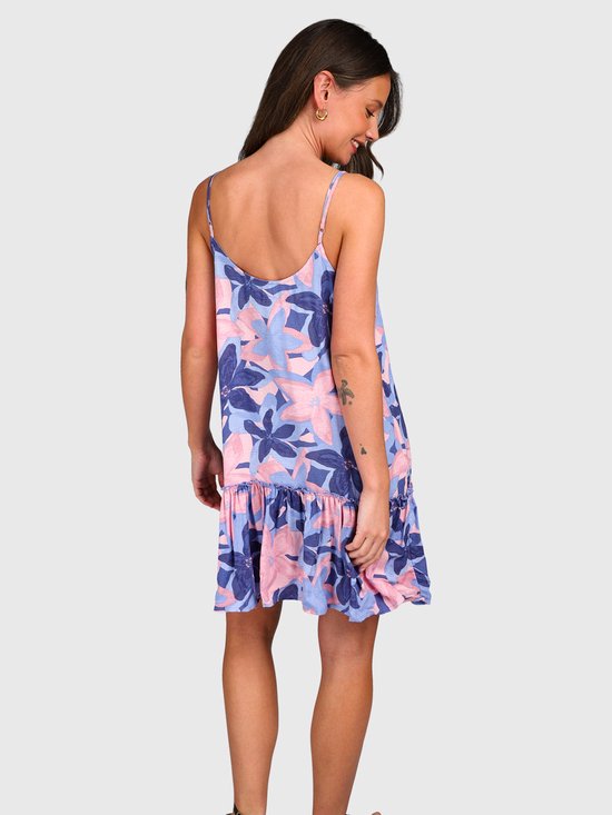 Une femme porte une robe ample à fines bretelles avec un imprimé floral bleu, rose et violet. Le dos de la robe a un volant au bas.