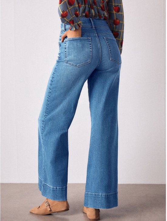 Model van achteren gezien, in een blauwe top met appelprint en gele ruit, met een hoge taille en wijde jeans.