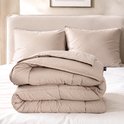Een beige dekbed is opgevouwen op een bed met twee beige kussens op de achtergrond.