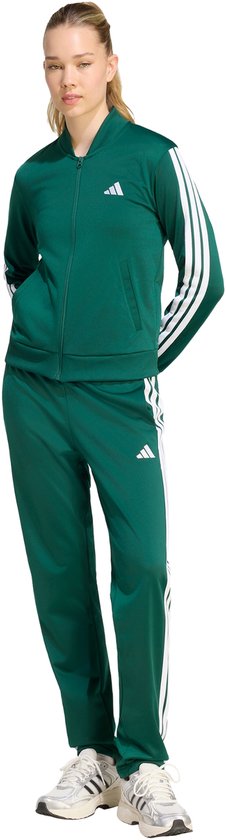 Vrouw in groen trainingspak met witte strepen, handen in de zakken.