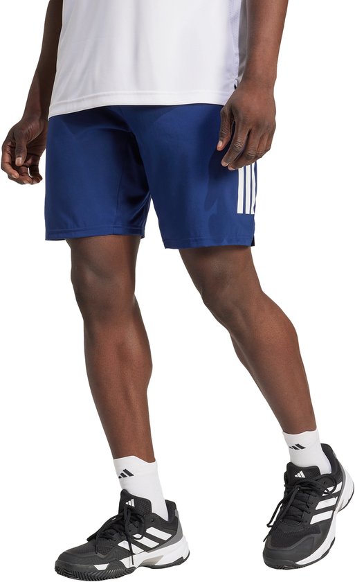 Man in een marineblauwe sportshort met witte Adidas strepen op het linkerbeen, witte sportsokken en zwarte tennisschoenen.
