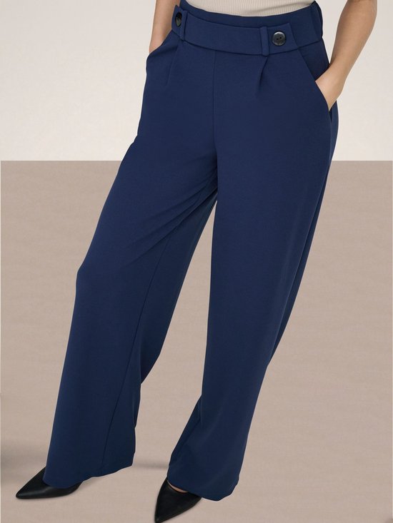 Model draagt donkerblauwe wijde broek met beige top.