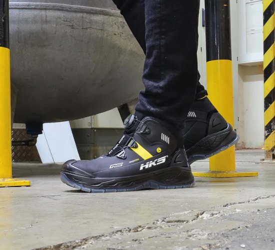 Persoon draagt hoge zwarte werkschoenen met gele streep en BOA sluiting.