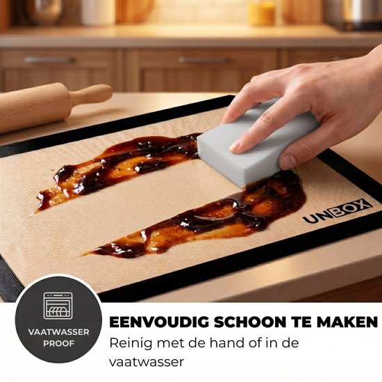 Een hand schuurt met een spons dikke, bruine saus van een beige bakmat met zwarte rand.