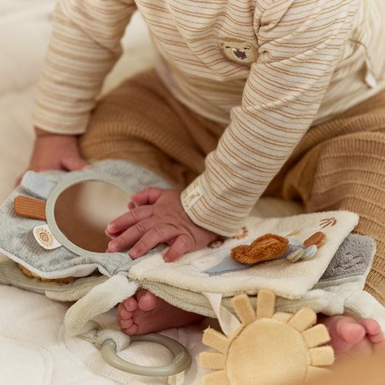 Baby ligt op de buik te spelen met het stoffen boekje. Opengevouwen boekje met spiegel, leeuw en flamingo.