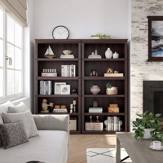 Twee donkerbruine boekenkasten met elk vijf planken, gevuld met decoraties, boeken en planten. In een woonkamer met open haard.