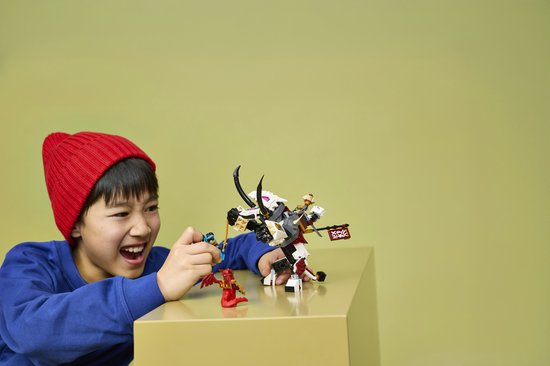 Jongen met rode muts speelt met LEGO NINJAGO speelgoed: een draakachtig beest met ruiter, een rode draak en een ninja met zwaard.