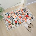 Een lichtroze kleed met een vol bloemenpatroon in rood, oranje, geel en blauw, gelegen bij een ingang met witte pantoffels.