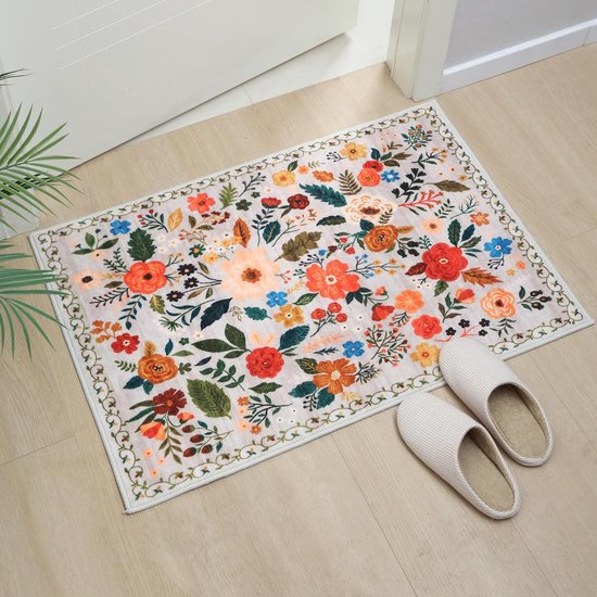 Een lichtroze kleed met een vol bloemenpatroon in rood, oranje, geel en blauw, gelegen bij een ingang met witte pantoffels.