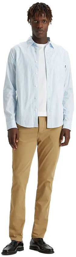 Man in een gestreepte lichtblauwe blouse, wit T-shirt en beige chino broek.