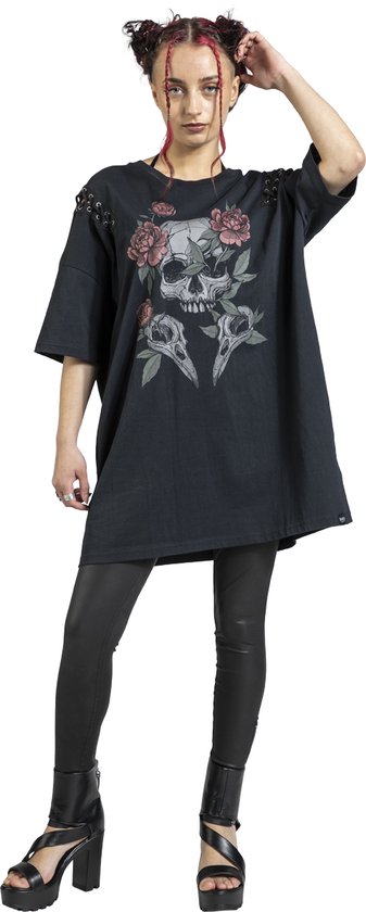 Vrouw in zwart oversized T-shirt met schedel- en bloemenprint, veters aan de schouders, zwarte legging en platformlaarzen.