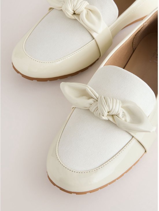 Close-up van off-white lakleren loafers met suède neus en strikdetail.