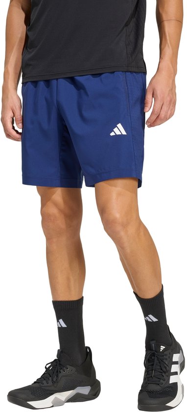 Model draagt een blauwe sportbroek met wit adidas-logo en zwart T-shirt en sportschoenen.