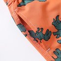 Detail van de zak van een oranje zwembroek met groene dino print en witte stiksels.