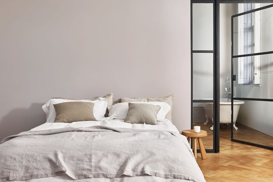 Slaapkamer met een opgemaakt bed, een kleine kruk en een glazen deur naar een badkuip.