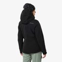 Vrouw met zwarte ski-jas, muts en groene broek, kijkend over de schouder.
