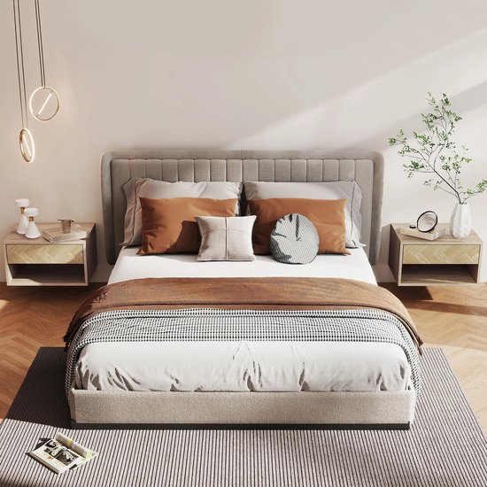Een tweepersoonsbed met grijze hoofdbord, met bruine en witte kussens en een bruine plaid. Twee zwevende nachtkastjes aan weerszijden met gouden lampen erboven.