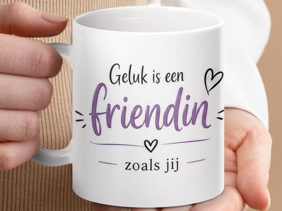 Witte mok met de tekst 'Geluk is een friendin zoals jij', vastgehouden door handen.