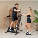 Man en vrouw op een zwarte crosstrainer, lachend naar elkaar.