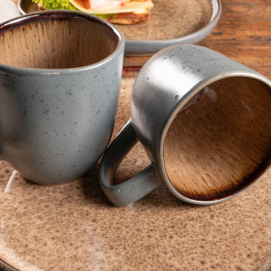 Twee grijze mokken, één staand, één liggend, met bruine binnenkant op een tafel.