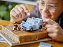 Une personne jeune portant des lunettes joue avec une Ford Anglia Lego bleu clair. Harry Potter, Ron Weasley, Hedwige et Croûtard sont des figurines, sur un livre.