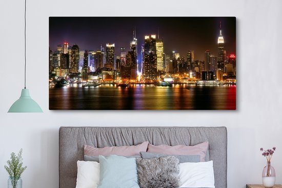 Une chambre avec une grande toile de la skyline de New York la nuit, au-dessus d'un lit avec des coussins.