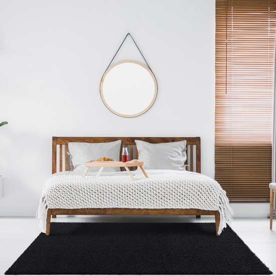 Tapis shaggy noir devant un lit en bois avec une couverture blanche et des coussins, dans une chambre.