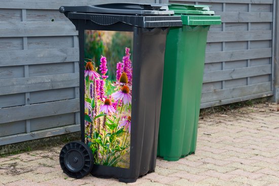 Zwarte afvalcontainer met sticker van roze echinacea en siergras, naast een groene container.