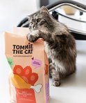 Grijze kitten met poten op een zak kattenvoer van Tommie The Cat. Zak met kip afbeelding, speciaal voor kittens.