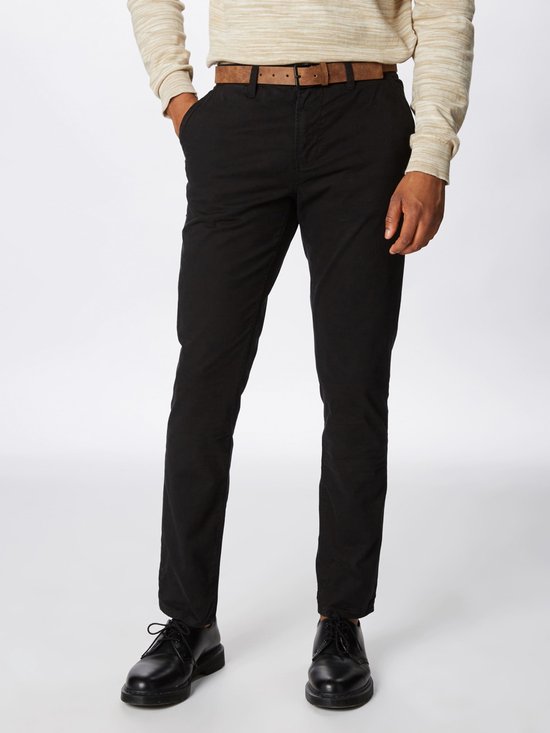 Man met zwarte chino broek, bruine riem en licht gestreepte trui.