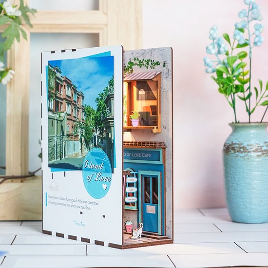 Boekensteun 'Island of Love' met miniatuur café-gevel en een straatscène op de achtergrond.