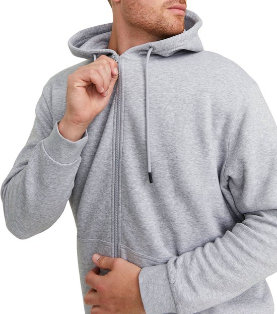 Man met lichtgrijze hoodie, rits gedeeltelijk geopend, grijze broek.