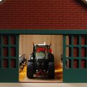 Binnenkant van een speelgoedboerderij met een groene tractor, rood-wit koeien en een groen dak.