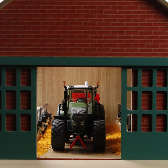 Binnenkant van een speelgoedboerderij met een groene tractor, rood-wit koeien en een groen dak.