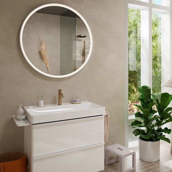 Badkamer met wastafel, gouden kraan, spiegel, plant en raam.
