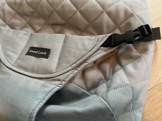 Detail van grijze, gewatteerde stoelhoes met een zwart label "Good Luck" en een gesp.