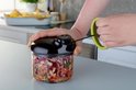 Een hand die de lus van een Tefal hakmolen trekt, met fijngesneden groenten in de container.